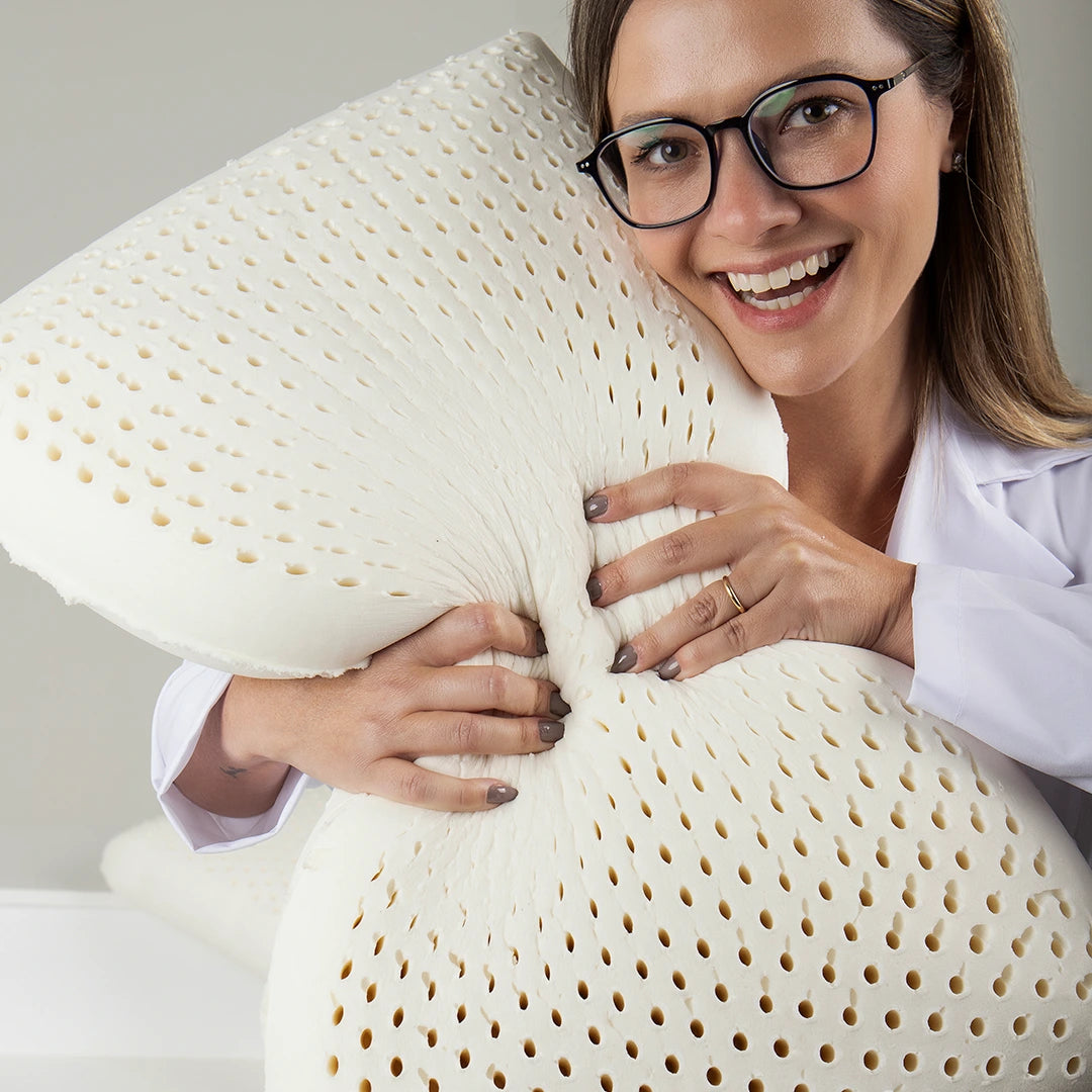 mulher com óculos sorrindo apertando o travesseiro IWS Original Látex® destacando sua maciez e conforto
