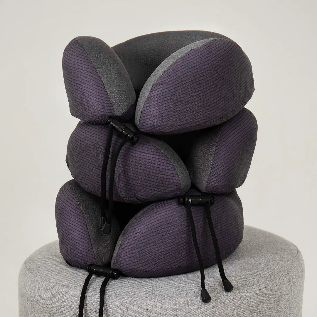 Três almofadas de pescoço Travel Pillow U - IWS Off Night empilhadas sobre um puff cinza, com fundo branco. Ideal para conforto e suporte em viagens.