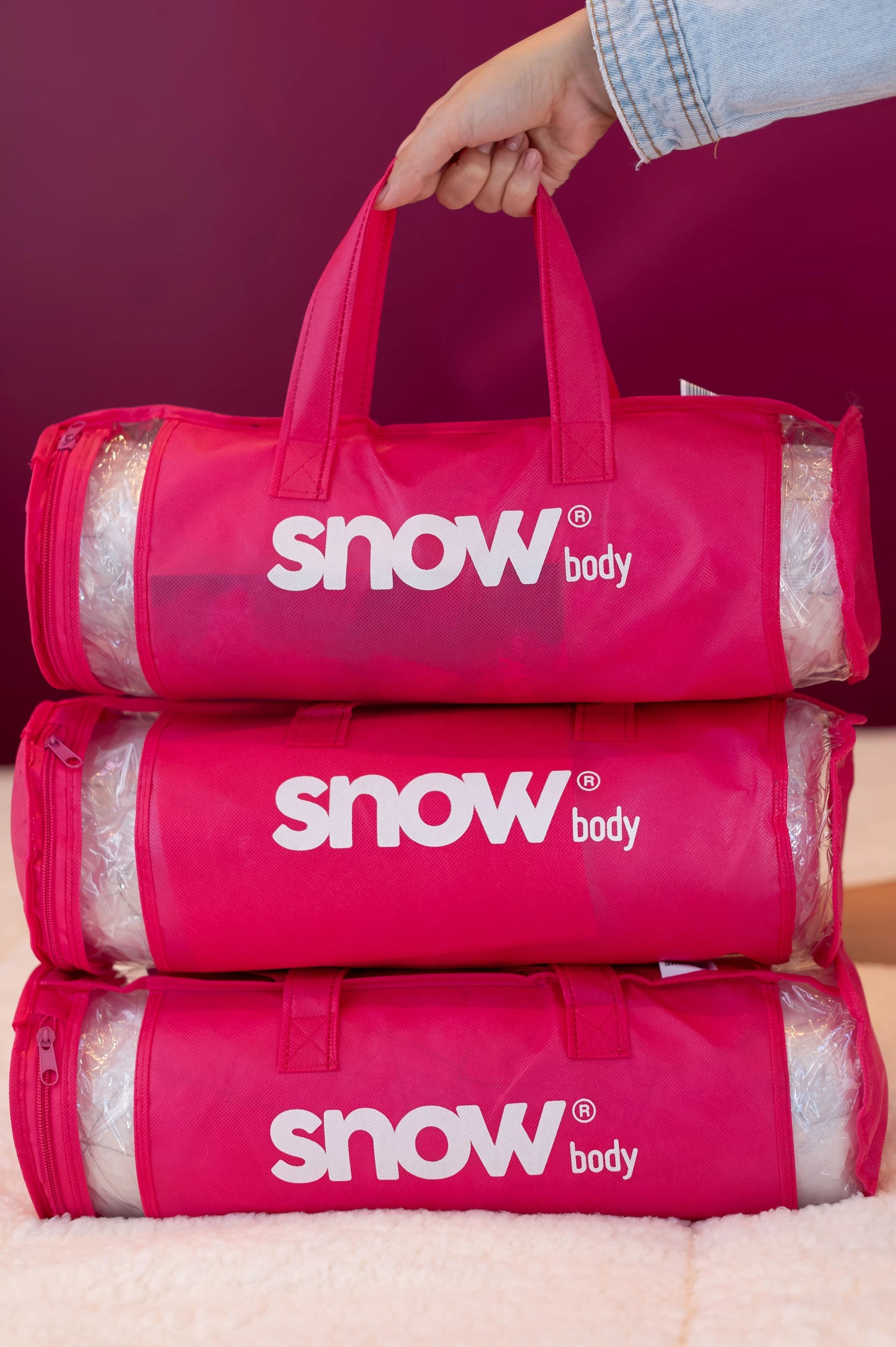 Três embalagens do Snow Body, travesseiro de corpo da i wanna sleep, embalagens são bags na cor rosa com a logo do travesseiro em branco