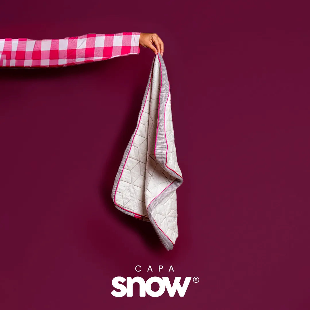Mão feminina vestida com pijama xadrez rosa e branco segurando no ar uma capa para travesseiro com zíper da i wanna sleep, fundo roxo e logo do produto na parte inferior da imagem