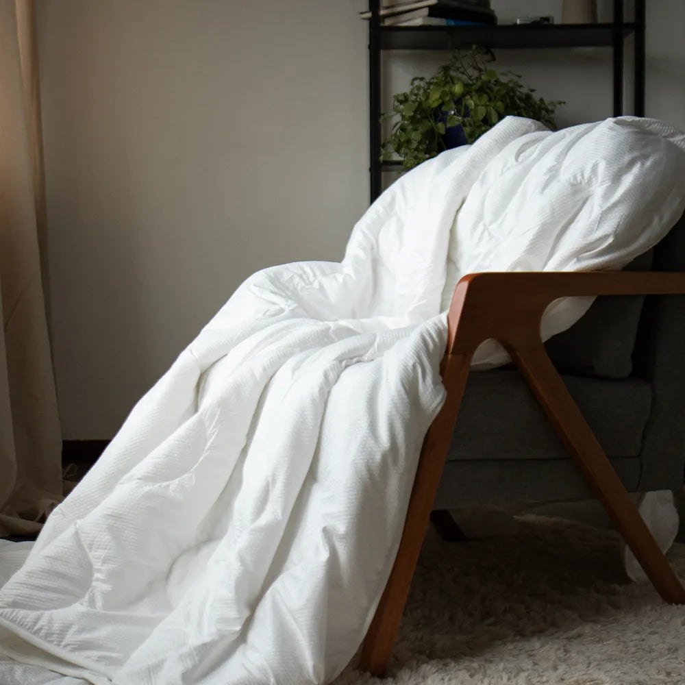 cobertor cozy da iws branco em cima de uma poltrona cinza com braços de madeira