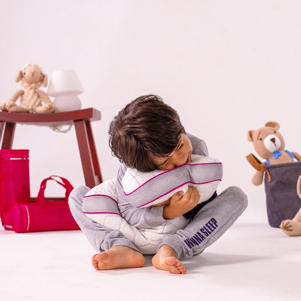 criança feliz vestindo pijama da i wanna sleep abraçando seu travesseiro infantil Snow kids em um espaço branco com brinquedos aos fundos