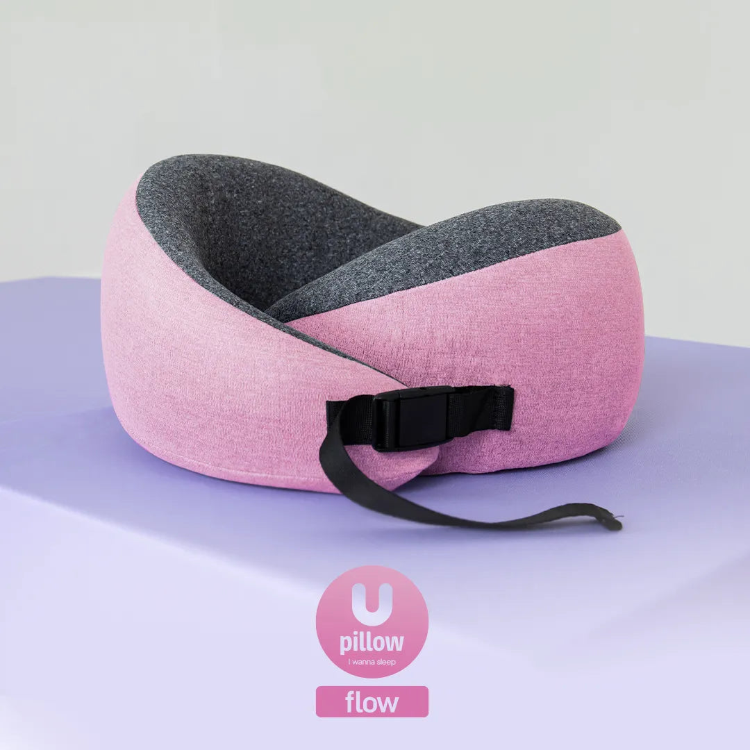 Travesseiro de pescoço Flow da I Wanna Sleep, na cor rosa, apoiado sobre uma superfície lilás com fundo branco, com o logo do produto na parte inferior da imagem.