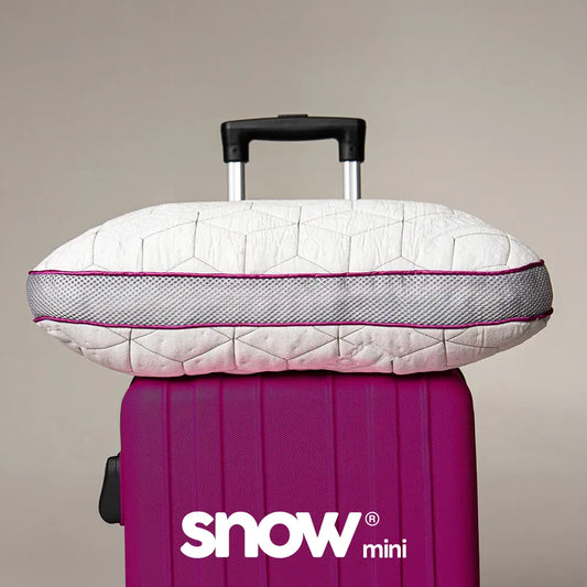 O travesseiro de viagem Snow Mini da I Wanna Sleep sobre uma mala de viagem roxa, pronto para garantir conforto e suporte ideais em qualquer destino