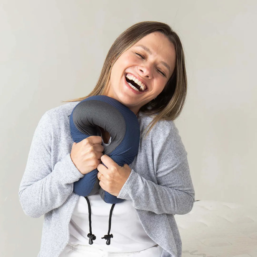 Mulher segurando a almofada de pescoço Travel Pillow U - IWS Off Night da i wanna sleep, sorrindo e  apertando ela demonstrando sua maciez que proporciona um conforto premium para viagens tranquilas