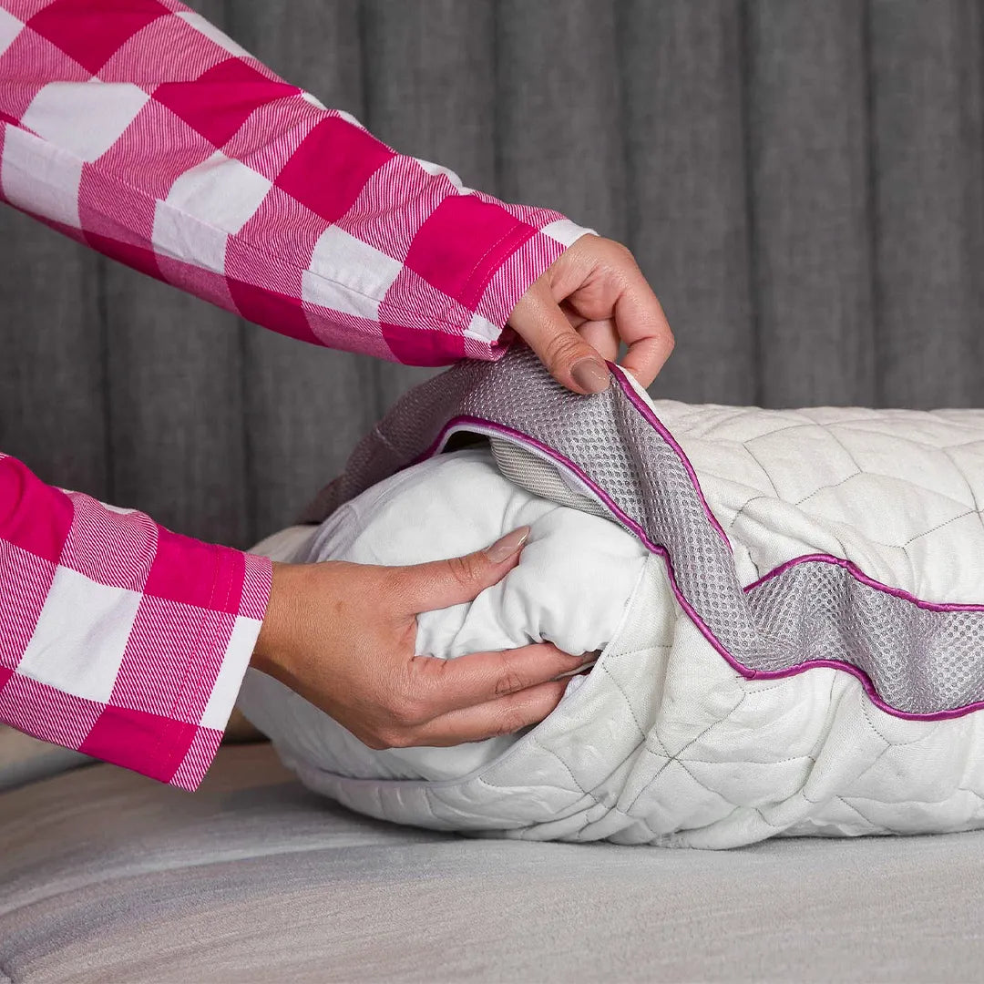 Mãos femininas com pijama xadrez  mostrando o travesseiro Snow dentro de sua capa feita com fibras de bambu, fundo cinza.