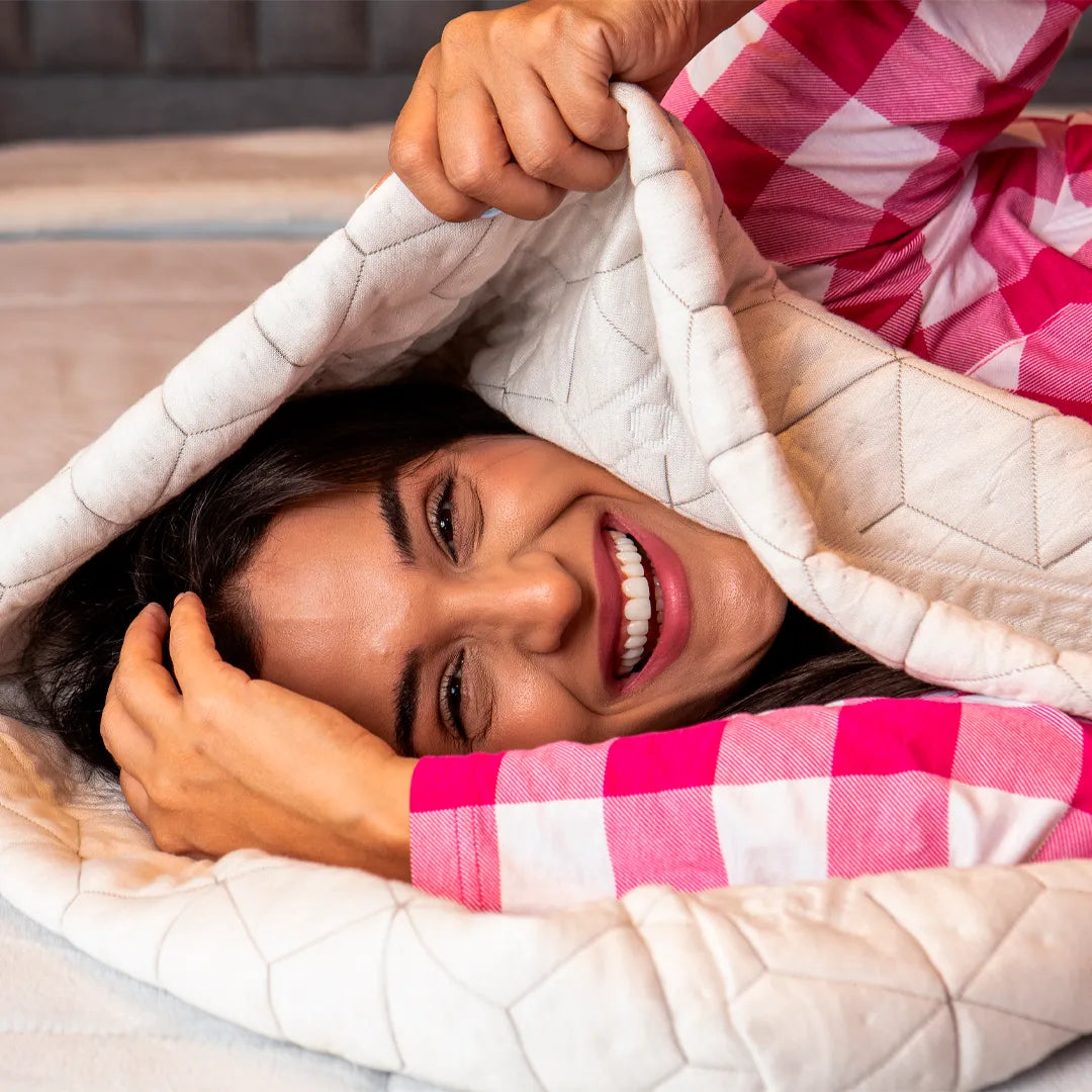 Mulher morena de pijama xadrez branco e rosa deitada na sua cama  envolvida com nossa capa para travesseiro de corpo Snow Body da IWS representando seu conforto e proteção