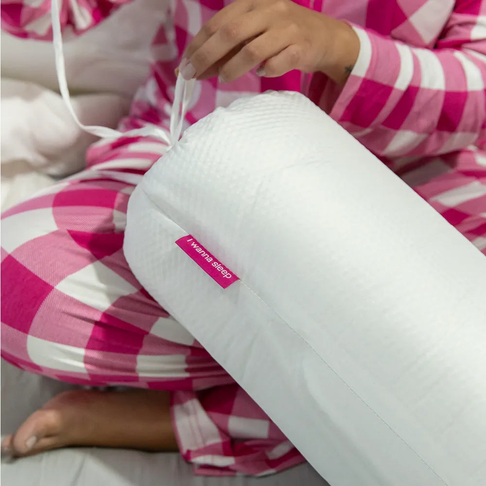 Mulher de pijama xadrez branco e rosa sentada em sua cama branca segurando a embalagem cinza do cobertor Cozy da i wanna sleep 