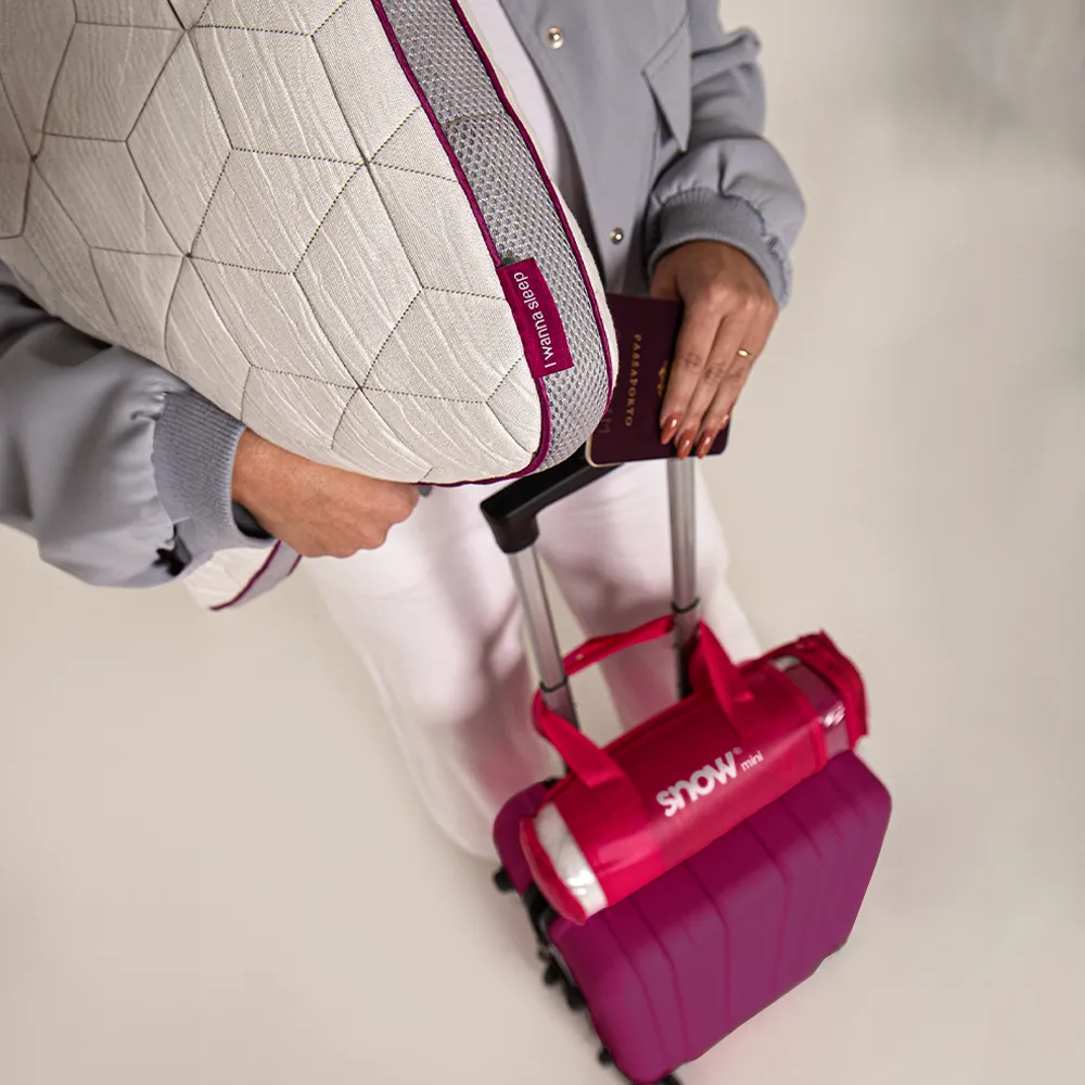 Mulher preparada para viajar com sua mala e travesseiro de viagem confortável e regulável, snow mini da i wanna sleep enquanto segura seu passaporte 