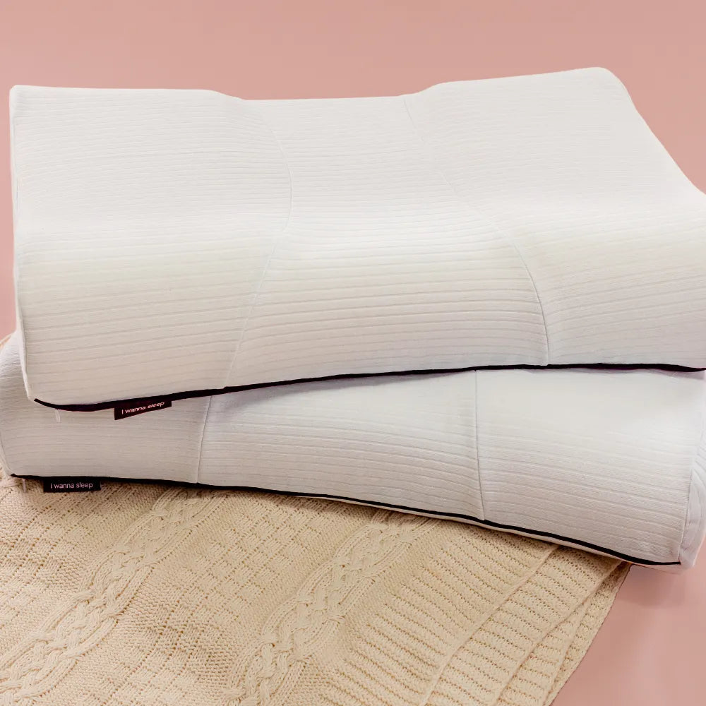 travesseiros duo position por cima de uma toalha macia, travesseiro ergonômico ideal para quem dorme de lado e de costas, imagem com fundo rosa destacando sua capa premium 100% algodão e de alta gramatura, que ajuda a transmitir um toque aconchegante, além de manter o travesseiro fresco durante a noite.