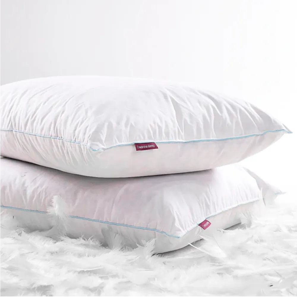O travesseiro pluma de ganso IWS, conforto premium que mantém sua maciez e forma original mesmo após longo uso, oferecendo conforto duradouro sem perder o suporte ideal. Na imagem temos dois travesseiro de pluma de ganso natural com sua capa confortável na cor branca, fundo branco e penas de ganso no chão da imagem